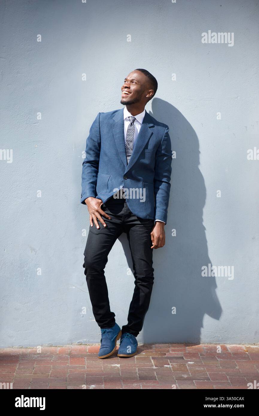 Ein junger nigerianischer Geschäftsmann lacht draußen und strahlt Vertrauen und Zugänglichkeit aus. Dieses Porträt in voller Länge eignet sich für Unternehmens-, Führungs- und Lifestyle-Branding. Ideal für geschäftliche, Networking- und Outdoor-Arbeiten. Stockfoto