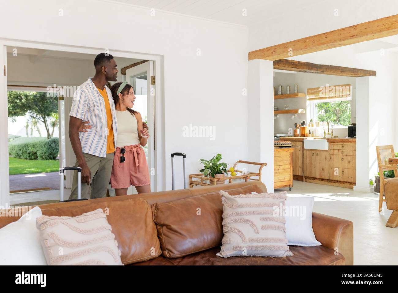 Diverse Paare betreten das Ferienhaus mit Gepäck, lächeln und erkunden gemütliches Wohnzimmer, Copy Spa Stockfoto