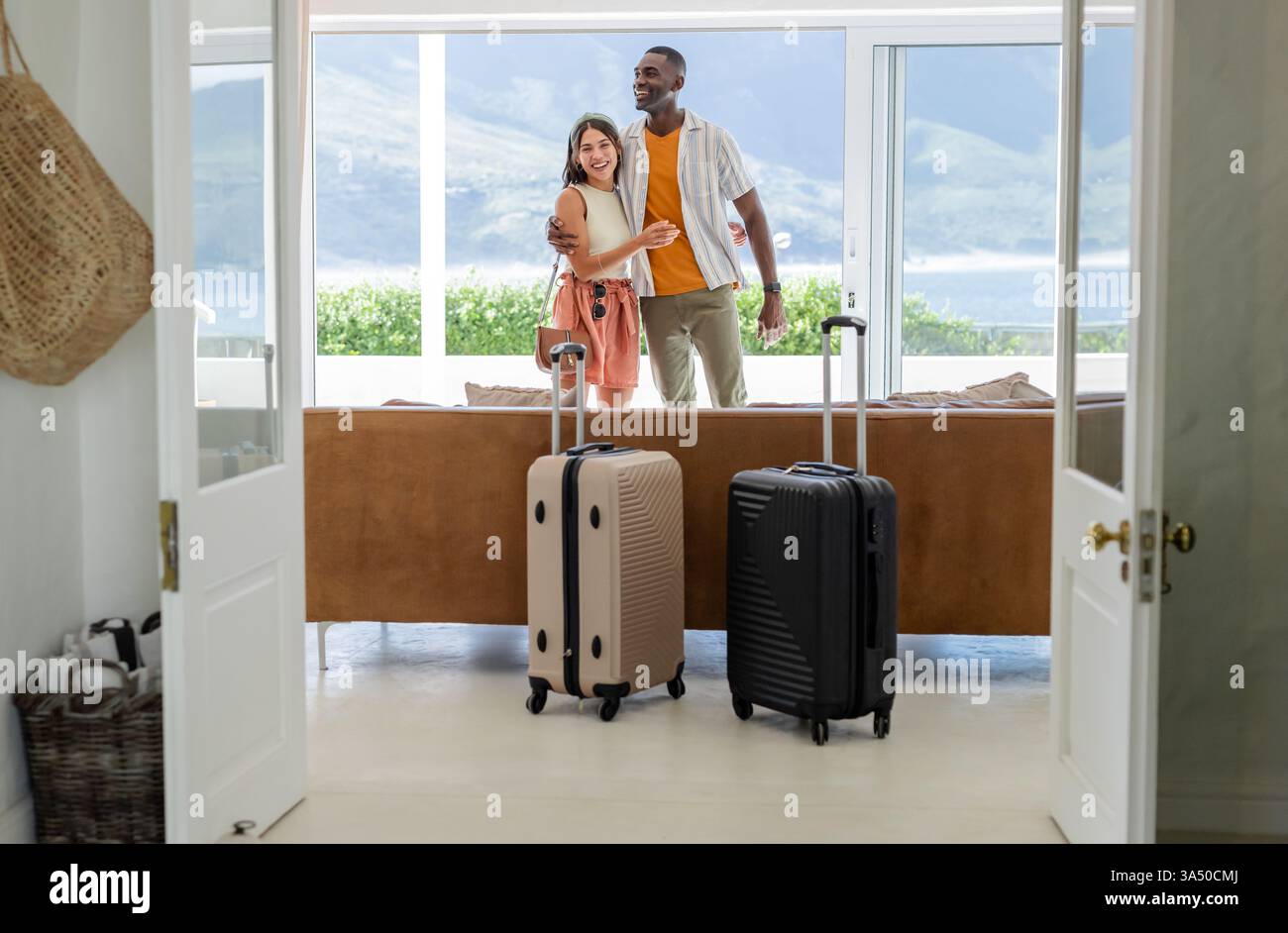 Glückliches, vielfältiges Paar, das sich im Wohnzimmer mit Koffern umschließt und den Urlaub genießt Stockfoto