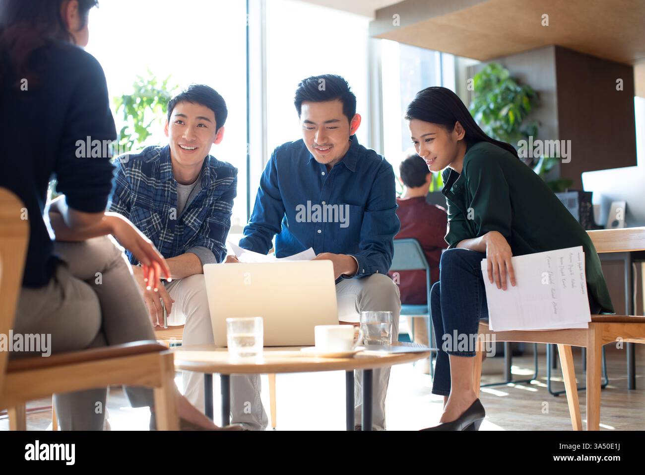 Lächelnde Gruppe von Menschen, die im Büro auf den Laptop schauen Stockfoto