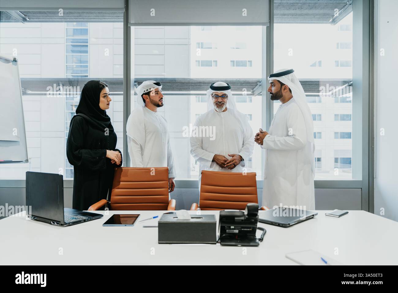Geschäftsleute aus dem Nahen Osten tragen Kandura und muslimische Geschäftsfrau in schwarzem Hijab, während sie zusammen vor dem Glasfenster stehen ... Stockfoto