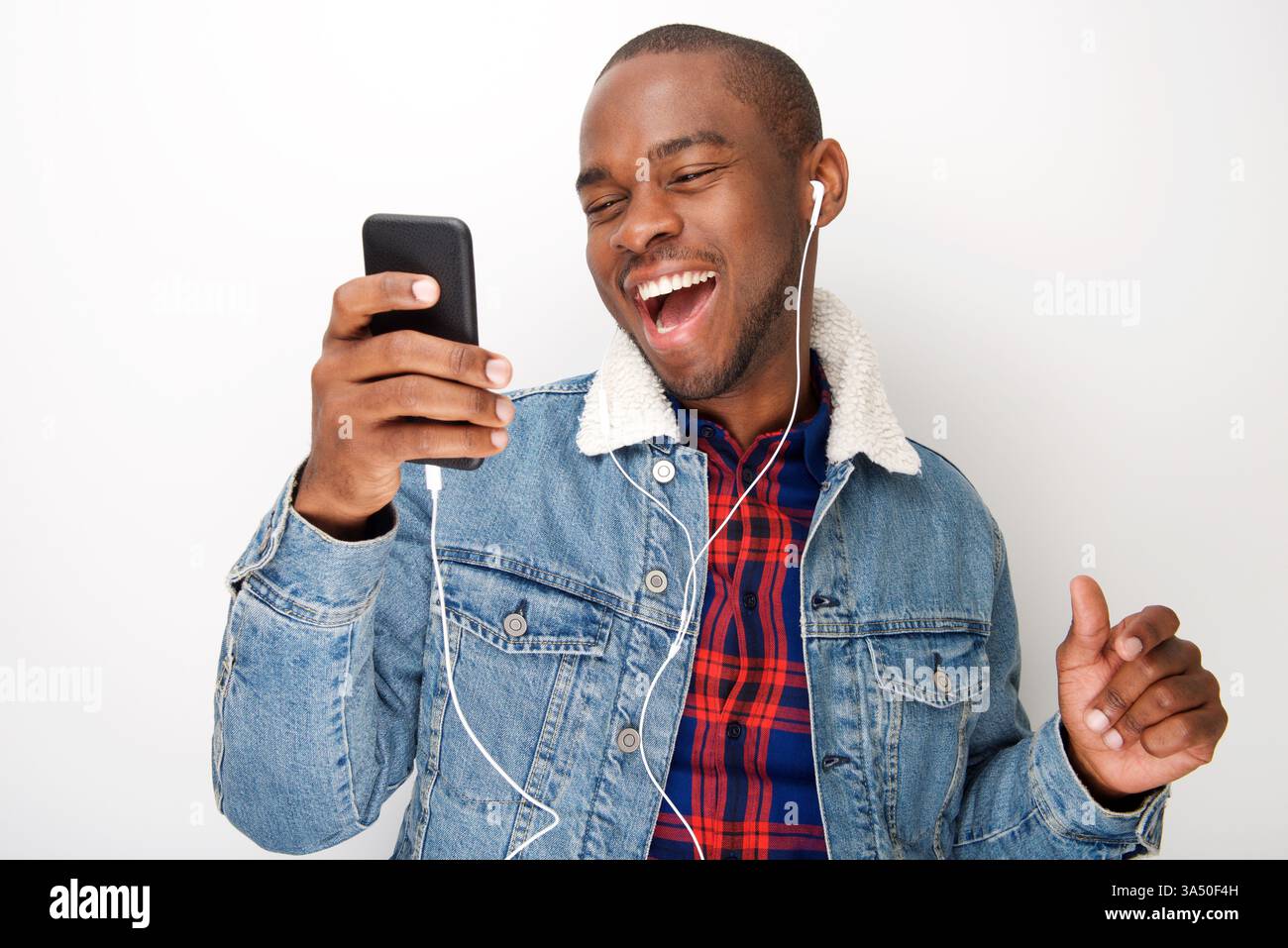 Lächelnder Schwarzer Mann, der Musik auf einem Smartphone mit Ohrhörern hört. Dieses fröhliche Lifestyle-Bild eignet sich ideal für Technologie-, Musik- oder Unterhaltungskontexte. Stockfoto