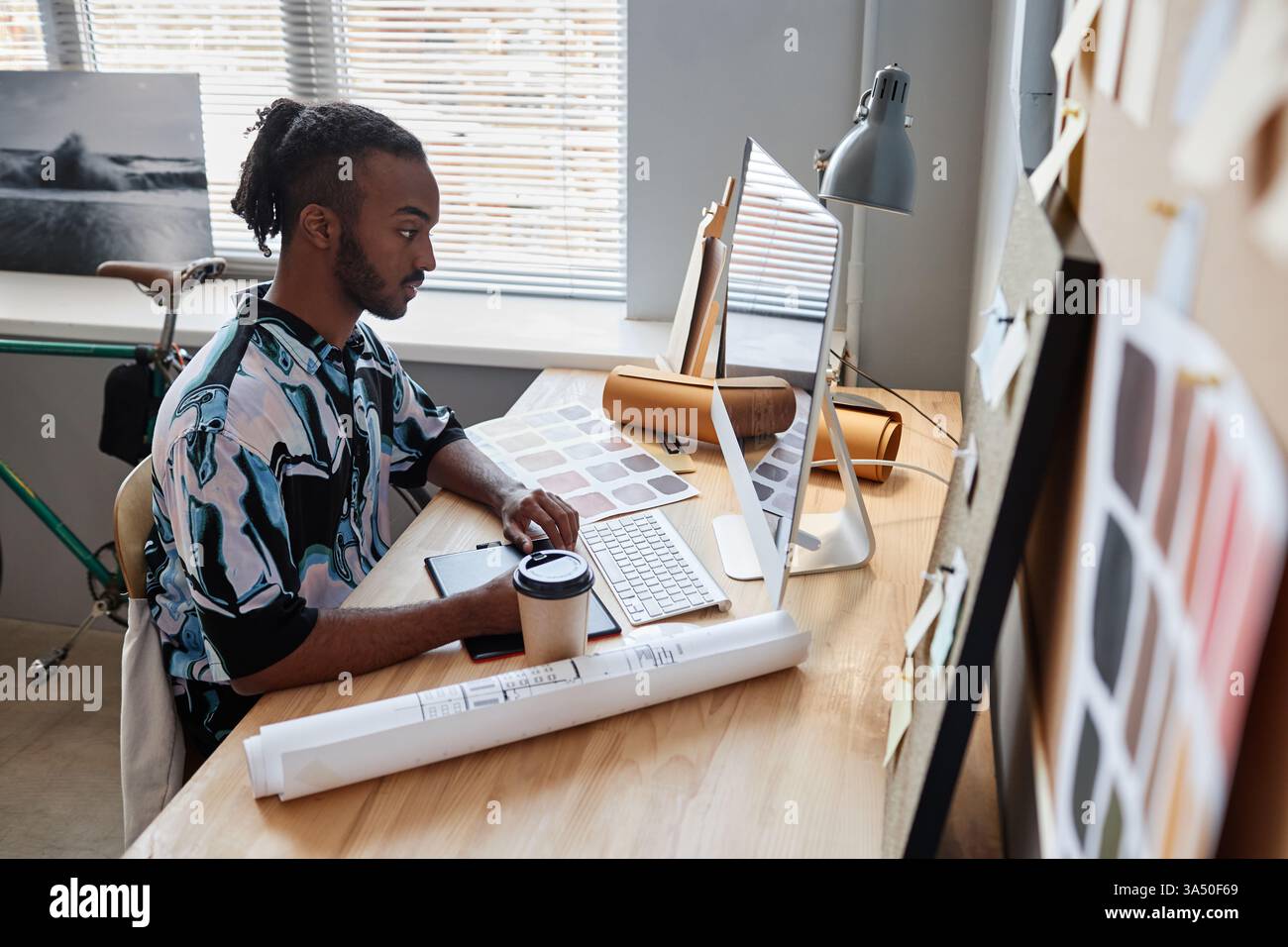 Seitenporträt eines jungen männlichen Mixed-Race-Designers bei der Arbeit in einem Home Office. Er sitzt an einem Schreibtisch mit Laptop und Stifttablett und signalisiert digitales Design und kreative Arbeit. Dieses Image eignet sich ideal für freiberufliche Design-, Innenarchitektur-, Architektur- und Remote-Arbeiten. Stockfoto
