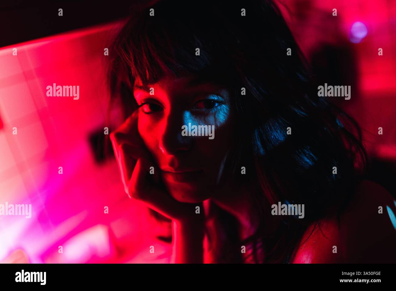 Eine hispanische Frau legt ihr Gesicht in einem schwach beleuchteten Raum zu Hause auf ihre Hand. Ideal für Lifestyle, Innenraumstimmung und zeitgenössisches Ambiente. Stockfoto