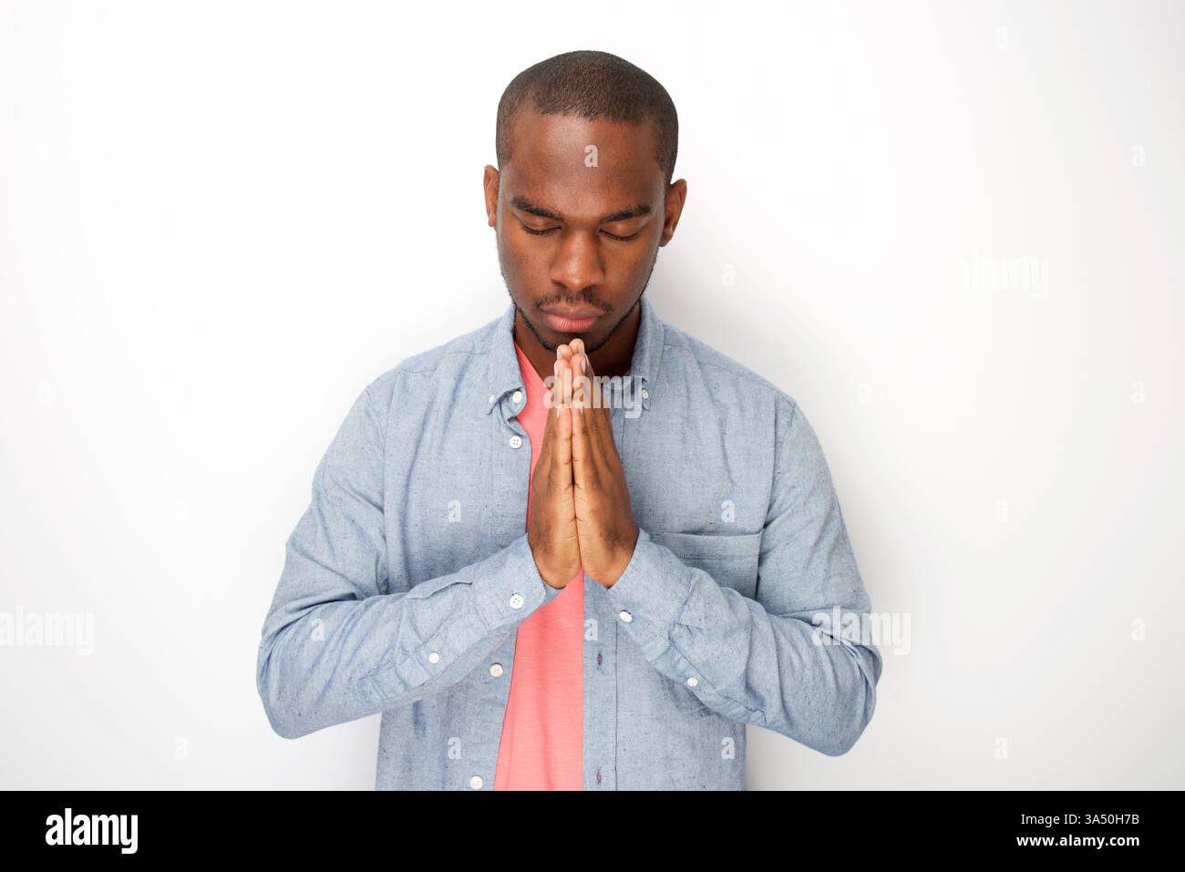 Heiterer afroamerikanischer Mann in betender Pose mit geschlossenen Augen vor einem sauberen weißen Hintergrund. Dieses Studio-Porträt vermittelt Ruhe, Aufrichtigkeit und Besinnung mit viel Platz zum Kopieren von Nachrichten. Ideal für Glaubens-, Meditations- und spirituelle Lebensstil-Kampagnen. Stockfoto