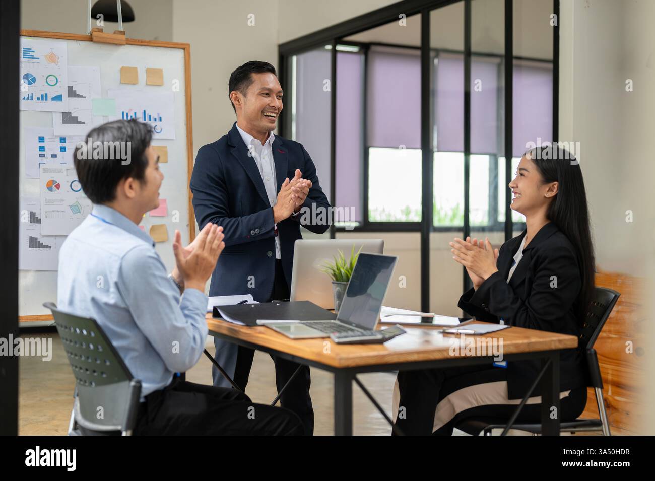 Gruppe asiatischer Geschäftsleute, die in einem Meeting klatschen und den Erfolg feiern. Eine Unternehmensszene, die sich perfekt für Teamarbeit, Führungsqualitäten und geschäftliche Erfolge eignet. Geeignet für Geschichten über Zusammenarbeit, Unternehmenswachstum und Feierlichkeiten am Arbeitsplatz. Stockfoto