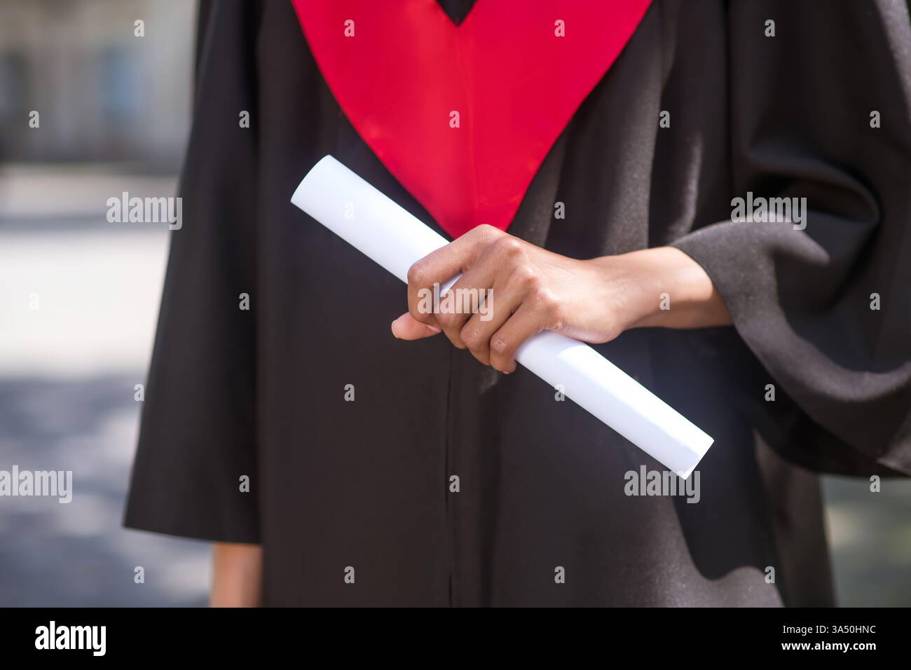 Afroamerikanische Frau im Abschlusskleid mit Diplom, die tagsüber draußen steht. Ein stolzer Moment für Absolventen, der für Kampagnen zu Bildung, Leistung und Erfolg von Studenten geeignet ist. Perfekt für Postgraduations- und Hochschulabschlüsse. Stockfoto