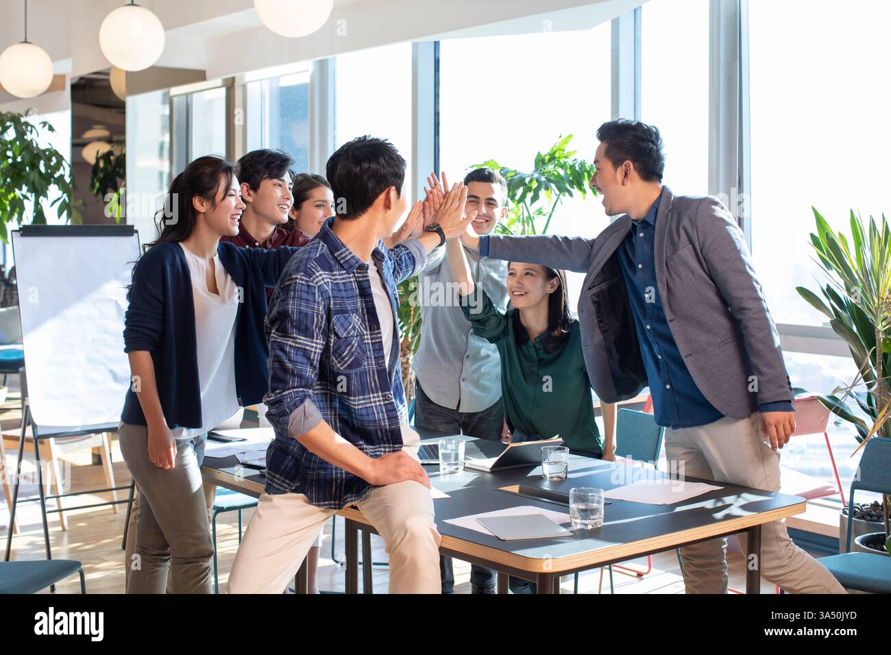 Fröhliche, vielfältige Gruppe von Geschäftsleuten, die High-Five im Büro machen Stockfoto