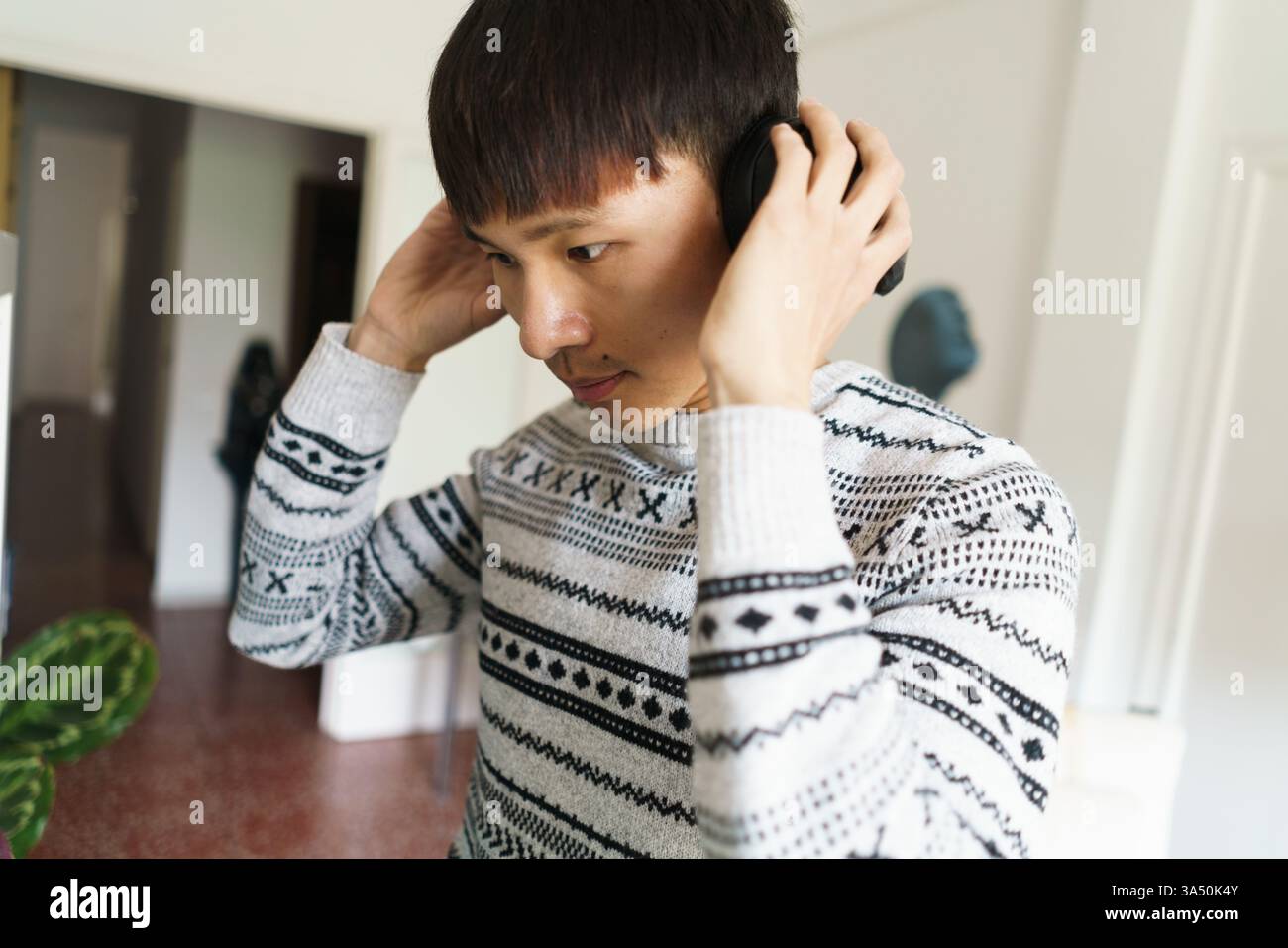 Ein asiatischer Mann hört zu Hause Musik und trägt Kopfhörer im Haus. Ein entspanntes Lifestyle-Image, das sich für Themen wie Technik, Unterhaltung und persönliches Wohlbefinden eignet. Stockfoto