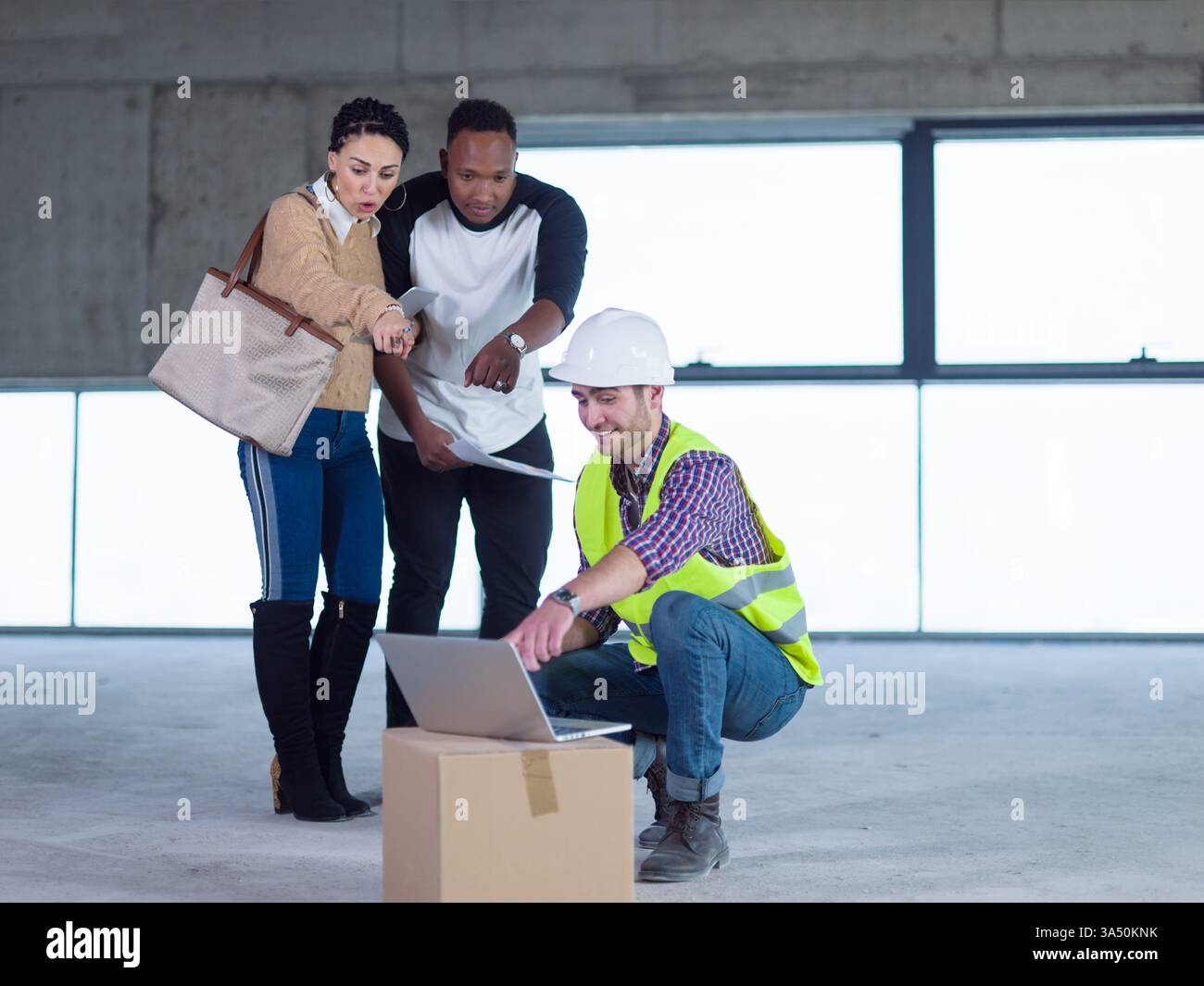 Verschiedene Gruppen stehen mit einem Tablet, während ein kaukasischer Ingenieur sich hockt, um die Pläne für die Hausgestaltung zu besprechen. Ein Bild mit dem Thema Bau und Architektur, das sich für Wohnbauprojekte eignet. Stockfoto