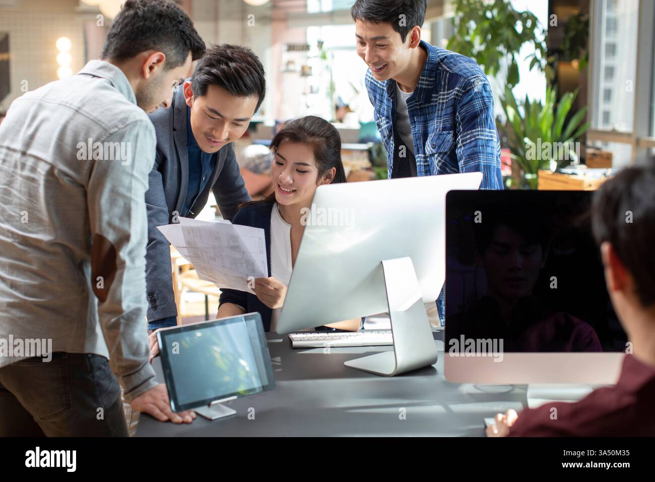 Lächelnde Gruppe von Geschäftsleuten, die vor dem Computer im Büro zusammenarbeiten Stockfoto