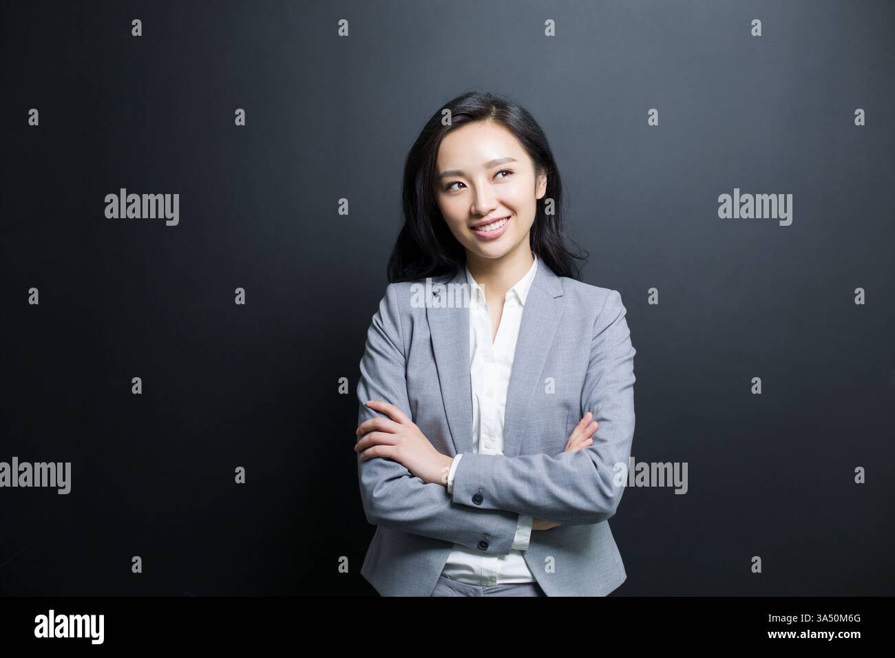Eine chinesische Geschäftsfrau im Anzug steht in einem Studio, tief in Gedanken mit einem kontemplativen Ausdruck. Diese Vorderansicht vor schwarzem Hintergrund vermittelt Professionalität und Fokus für Unternehmens-, Führungs- oder ideenorientierte Kampagnen. Stockfoto