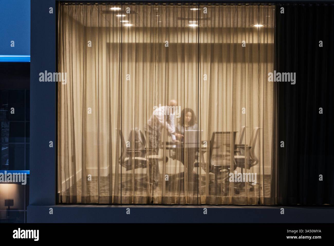 Zwei asiatische Profis, ein Geschäftsmann und eine Geschäftsfrau, arbeiten nachts in einem Konferenzraum. Eine Büroumgebung im Innenbereich, ideal für Unternehmenskommunikation, Teamarbeit und spätabendliche Meetings. Das Bild betont die Zusammenarbeit und den professionellen Fokus. Stockfoto