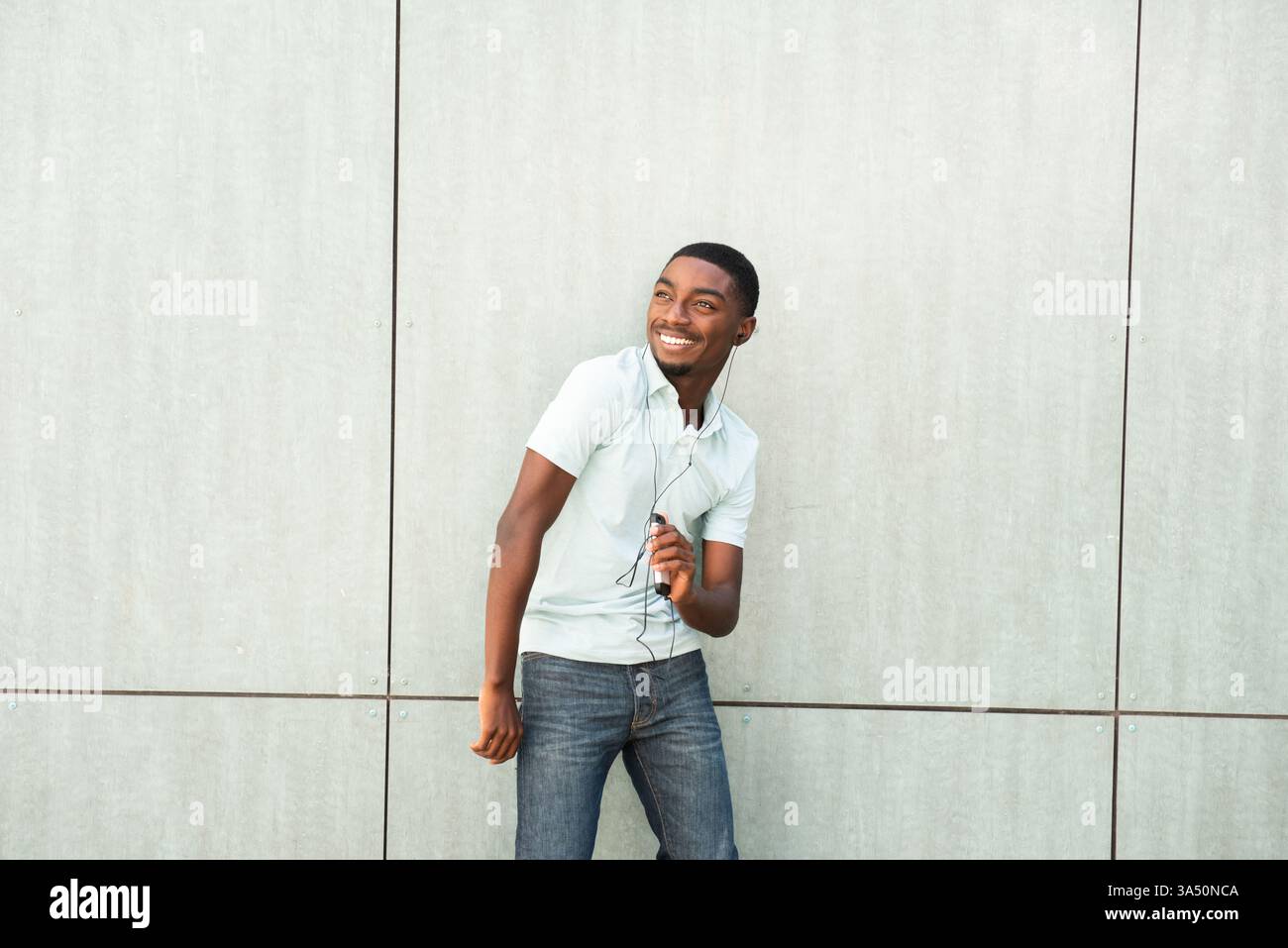 Porträt eines glücklichen jungen afroamerikanischen Mannes, der Musik mit Ohrstöpseln hört, während er ein Smartphone verwendet. Lässiges Lifestyle-Image, ideal für Musik-, Technologie- und Jugendkultur-Kampagnen. Perfekt für Lifestyle, Unterhaltung und Technologie. Stockfoto