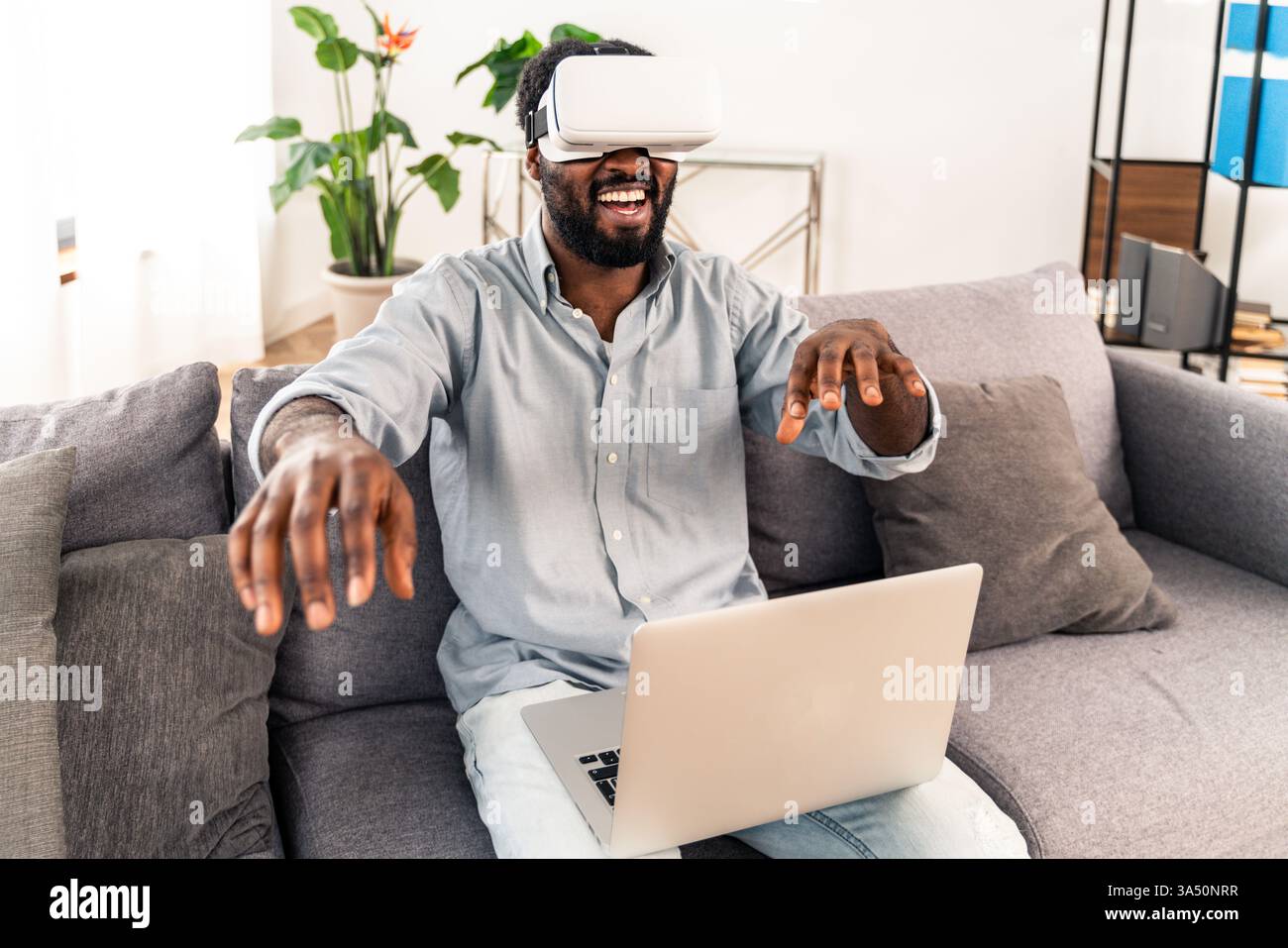 Gutaussehender Schwarzer Mann zu Hause, der mit einem Virtual-Reality-Headset spielt. Entspanntes Wohnzimmer mit modernster Lifestyle-Atmosphäre. Perfekt für Gaming-, Technologie- und Home Entertainment-Kampagnen. Stockfoto