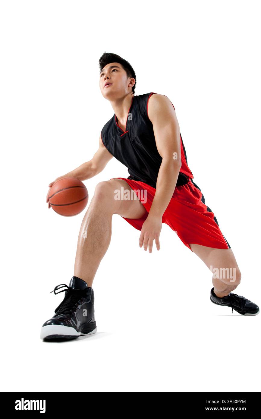 Ein chinesischer Mann, der einen Basketball in einem Studio dribbelt. Der fokussierte Athlet zeigt Agilität und Engagement für den Sport. Perfekt für Sportbekleidung, Training und Basketball-Aktionen. Stockfoto