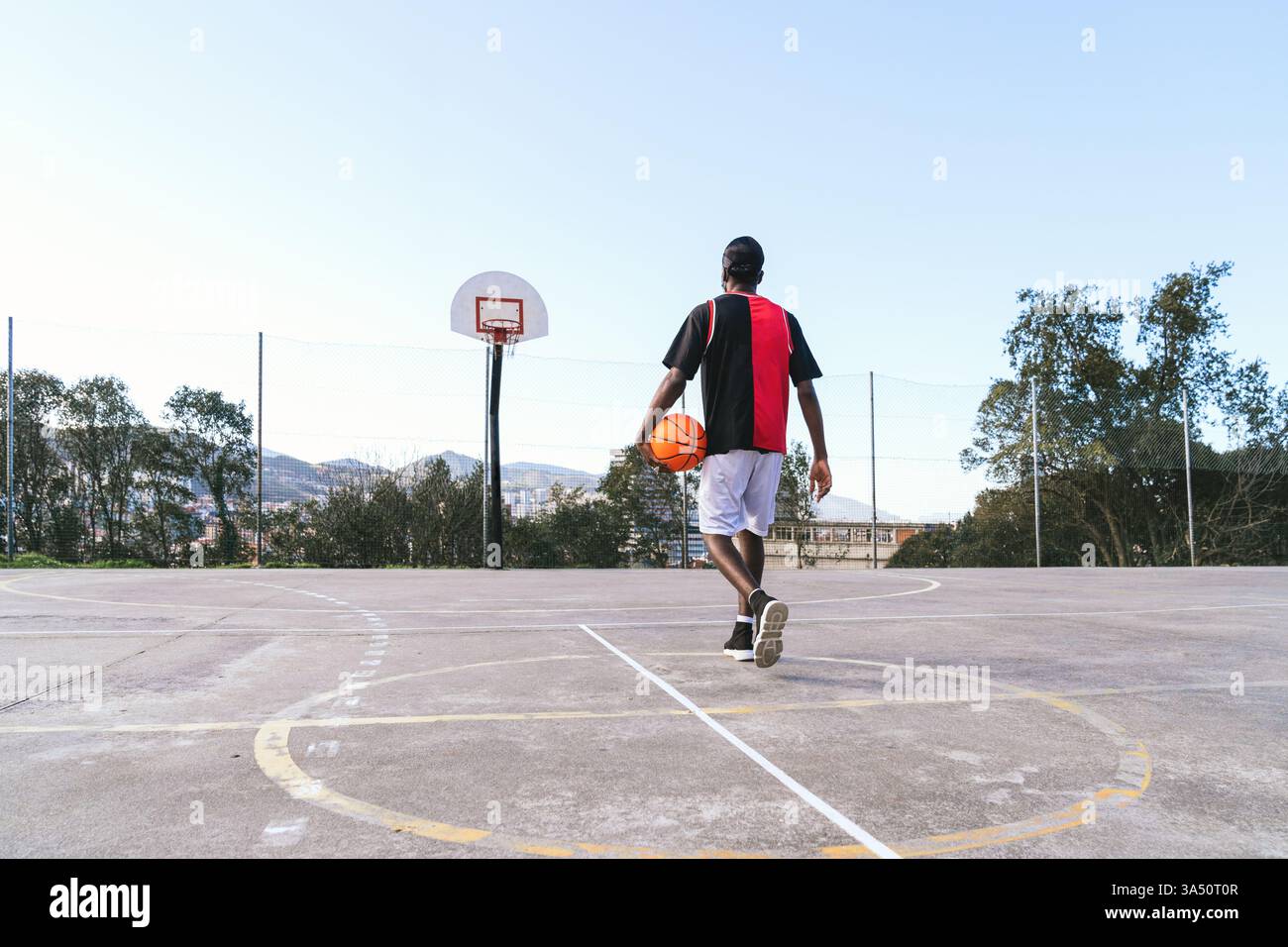 Junger schwarzer Basketballspieler in Uniform läuft mit Ball auf dem Platz. Die Szene vermittelt Sportlichkeit und Konzentration in einer sportlichen Umgebung. Ideal für Teamsport, Wellness und urbane Leichtathletik. Stockfoto