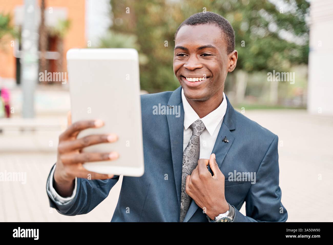 Ein afroamerikanischer Geschäftsmann steht in der Stadt und führt ein Videogespräch auf einem Tablet. Ideal für Geschäftskommunikation, Fernarbeit und digitale Technologie in städtischen Umgebungen. Ein professionelles, modernes Porträt, das die Konnektivität unterstreicht. Stockfoto