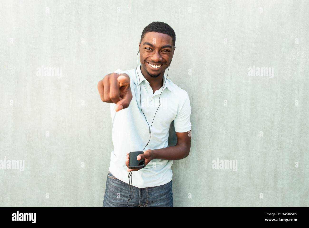Fröhliches Porträt eines jungen Schwarzen Mannes, der lacht, während er ein Mobiltelefon mit schnurlosen Ohrstöpseln benutzt. Ein lebendiges Lifestyle-Image, das sich für Technologie-, Musik- und mobile Kommunikationskampagnen eignet. Stockfoto