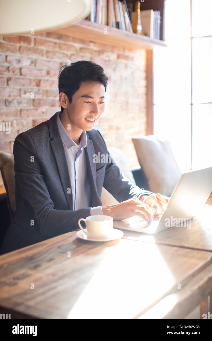 Chinesischer Geschäftsmann, der einen Laptop an einem Tisch in einem Café benutzt. Das zwanglose Arbeitsumfeld hebt die Kultur des Remote- oder mobilen Arbeitens und Cafés hervor. Stockfoto