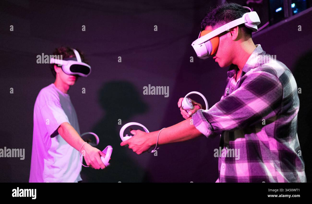 Seitenansicht von zwei Freunden in einem neonbeleuchteten Spielbereich mit VR-Headsets und beweglichen Controllern. Ein dynamisches Bild für virtuelle Realität, Spiele und immersive Unterhaltung. Stockfoto