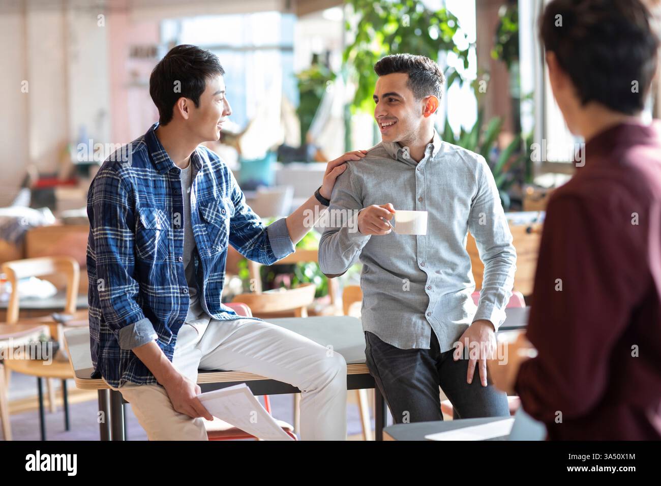 Lächelnde Gruppe von Geschäftsleuten, die miteinander reden, während sie eine Tasse Kaffee trinken und im Büro stehen Stockfoto