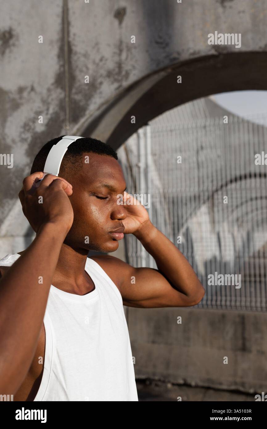 Entspanntes Porträt eines afroamerikanischen Mannes mit geschlossenen Augen, der Musik über Kopfhörer genießt. Ideal für Wellness, Fitness und Unterhaltung Lifestyle Bilder. Stockfoto