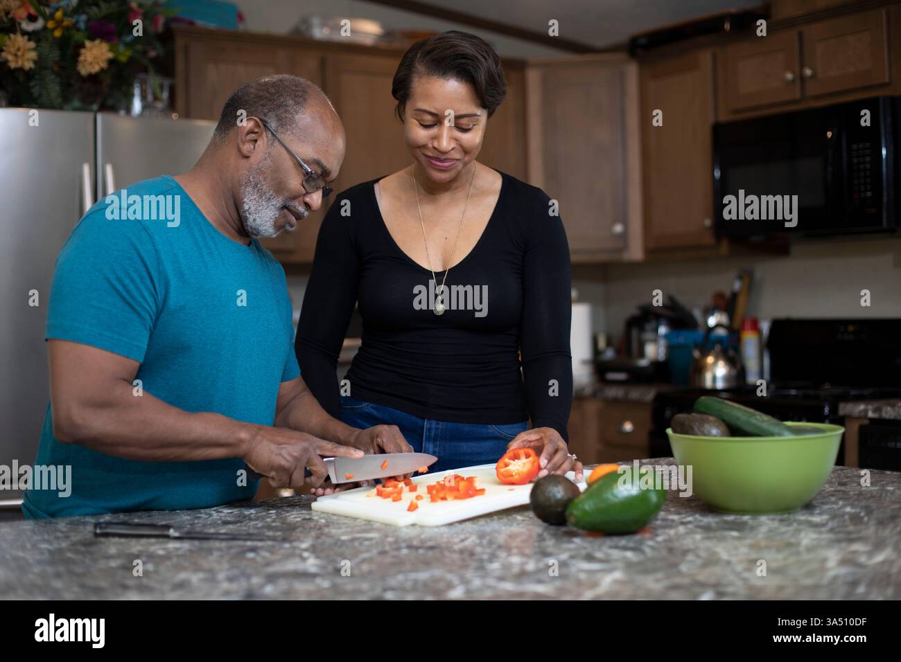 Hispanische und schwarze Paare kochen zusammen in einer modernen Küche. Dieses interrassische Duo teilt einen warmen, alltäglichen Moment der Zubereitung einer Mahlzeit. Ideal für das Familienleben, multikulturelle Beziehungen und Bilder zur Hausmannskost. Stockfoto