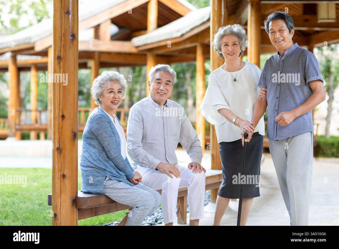 Lächelnde chinesische Freunde genießen einen entspannten Moment in einem Pavillon im Freien. Die Szene zeigt Freundschaft und Wohlbefinden unter älteren Erwachsenen in einem ruhigen Park in Peking mit Bäumen und einer Bank. Ein einladendes Lifestyle-Image, das sich für Altern, Ruhestand und aktive Seniorenwohnungskampagnen eignet. Stockfoto