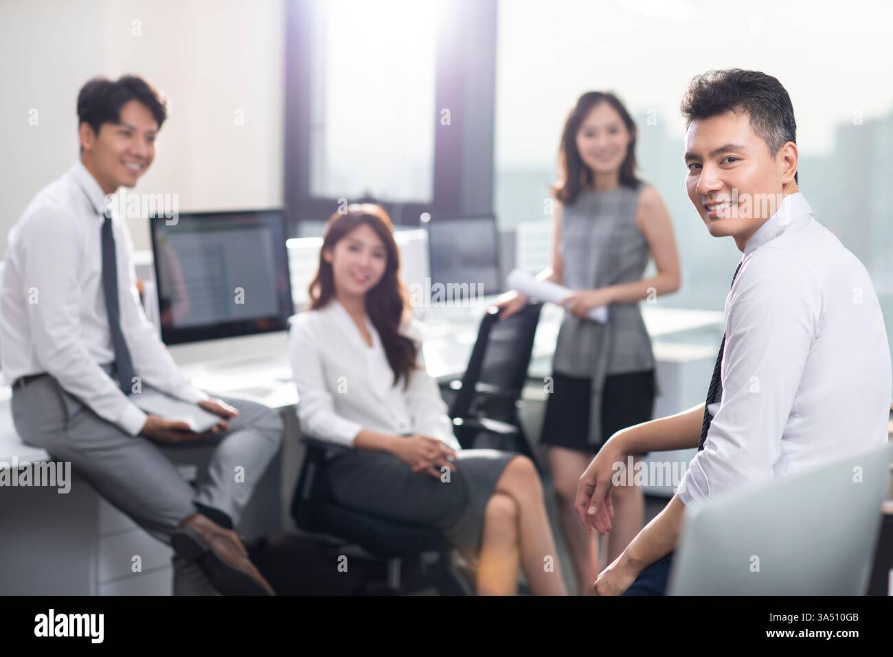 Ein lächelndes chinesisches vierköpfiges Team sitzt zusammen in einem hellen Büro. Unternehmensimage der Gruppe, das Teamwork, Zusammenarbeit und Kameradschaft am Arbeitsplatz betont. Professionelle Büroumgebung mit einem Gefühl von Einheit und Produktivität. Stockfoto