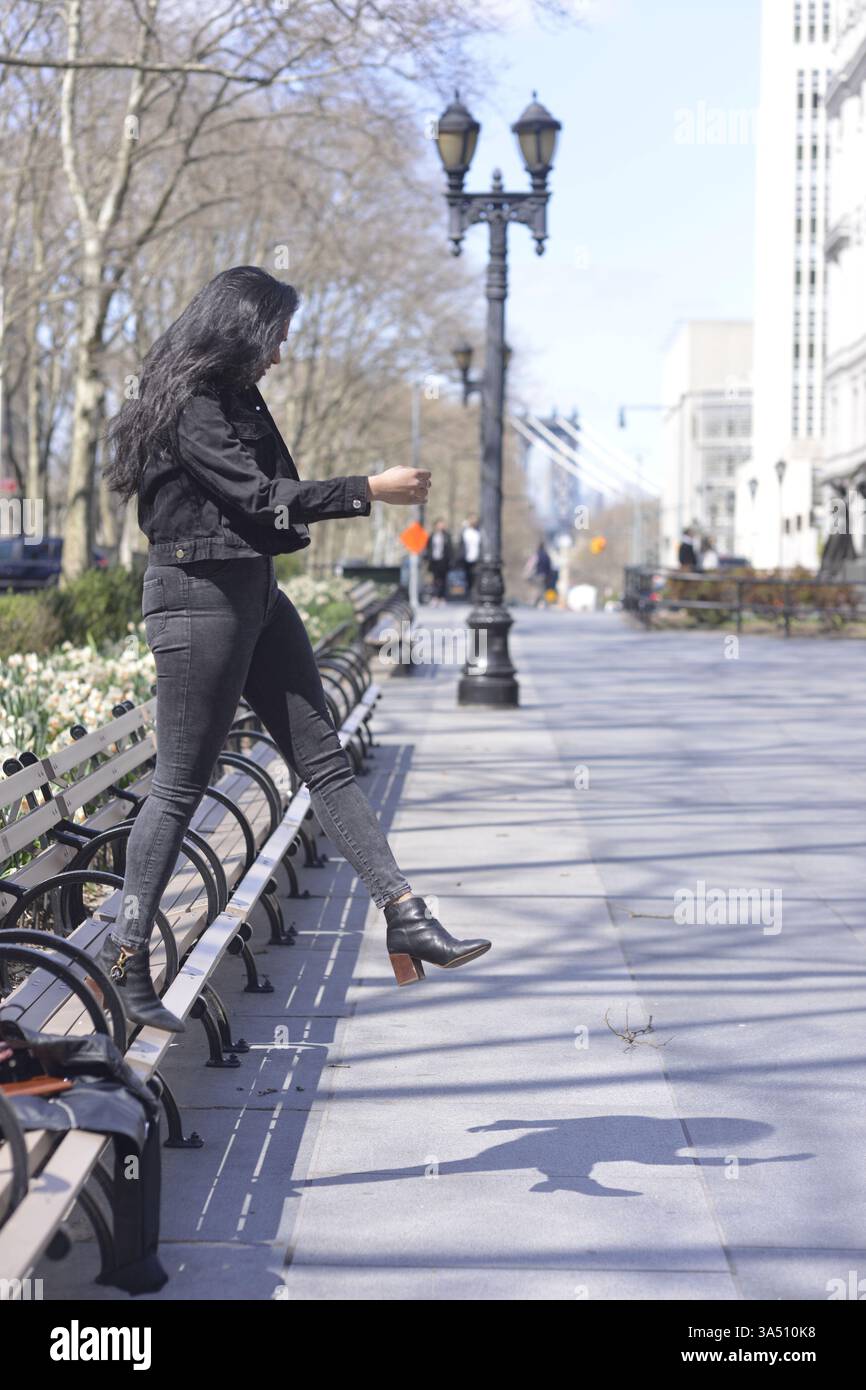 Indische Frau, die in der Stadt spaziert, lächelt und nach vorne blickt. Urbaner Lifestyle-Moment mit einem Hauch von winterlichem Stil und Bewegung. Ideal für das Stadtleben, Reisen und zeitgenössische Modeschöpfe. Stockfoto