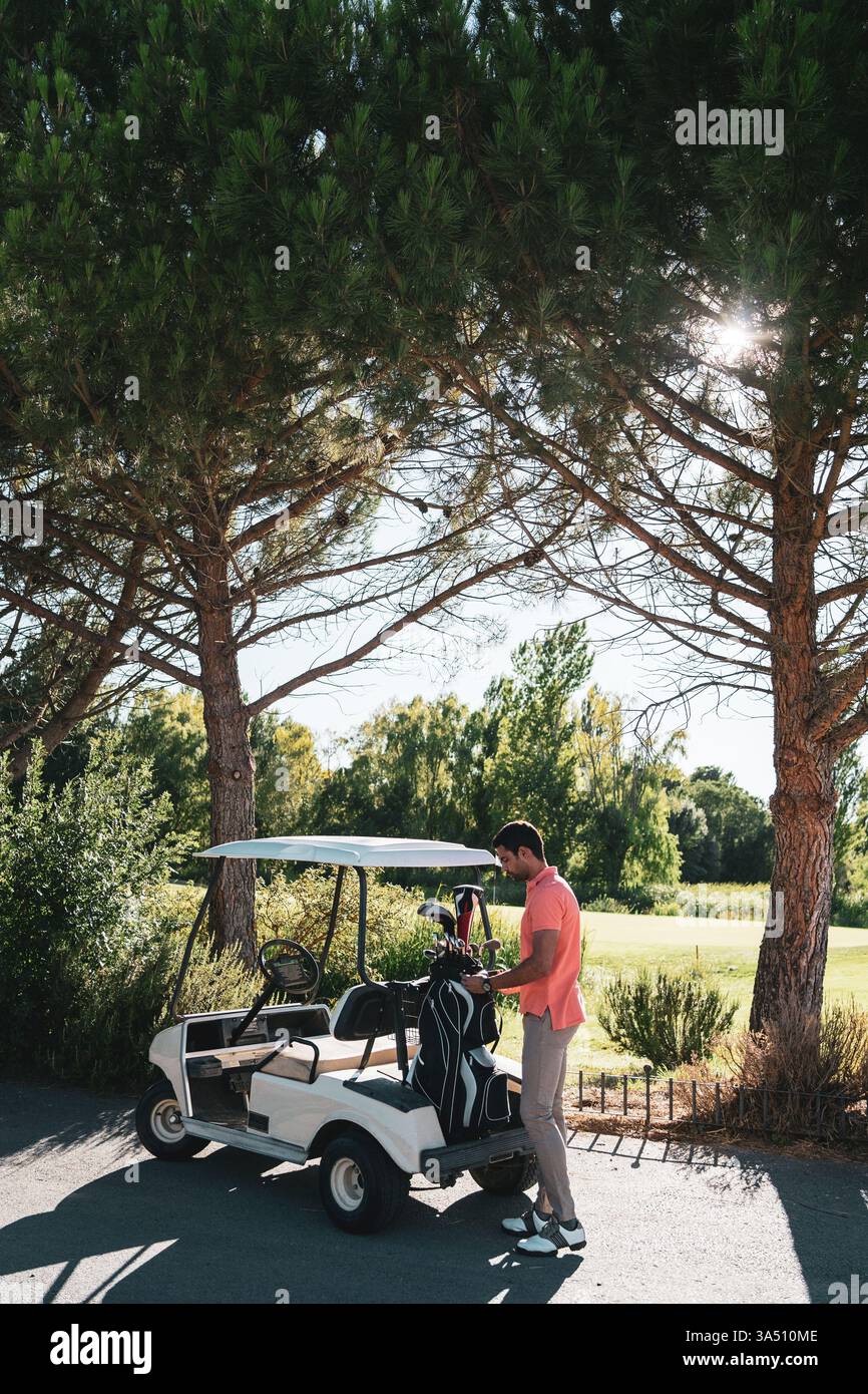 Ein männlicher Hispanic-Golfspieler steht bei Sonnenuntergang in der Nähe eines Golfwagens auf einem üppigen Golfplatz und bereitet sich auf den Putt vor. In dieser Szene werden Golfausrüstung, Sport und Freizeit für Sportmarketing oder Reiseangebote vorgestellt. Stockfoto
