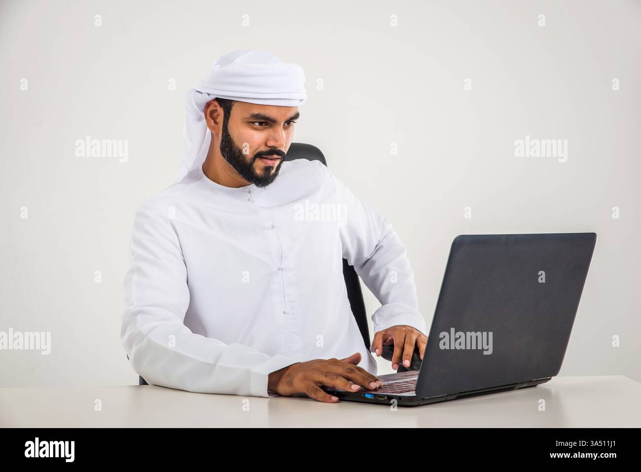 Mann aus dem Nahen Osten in traditioneller Emirat-Kandura posiert in einem Fotostudio. Sauberes Lifestyle-Porträt, geeignet für geschäftliche und regionale Kulturkampagnen. Ideal für den Einsatz im Unternehmens-, Familien- und Lifestyle-Marketing. Stockfoto