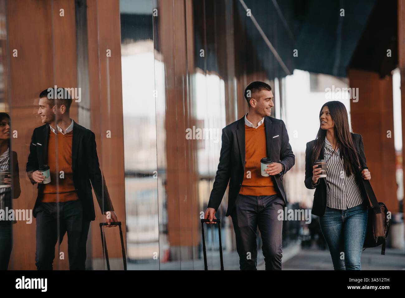 Fröhliche hispanische Frau und kaukasischer Geschäftsmann auf einer Geschäftsreise, zusammen zu Fuß in einem Flughafen mit Kaffee und Gepäck. Ideal für Reisen, internationale Geschäfte und verschiedene Teams. Perfekt für Geschäftsreisen, Meetings unterwegs und multiethnische Zusammenarbeit. Stockfoto