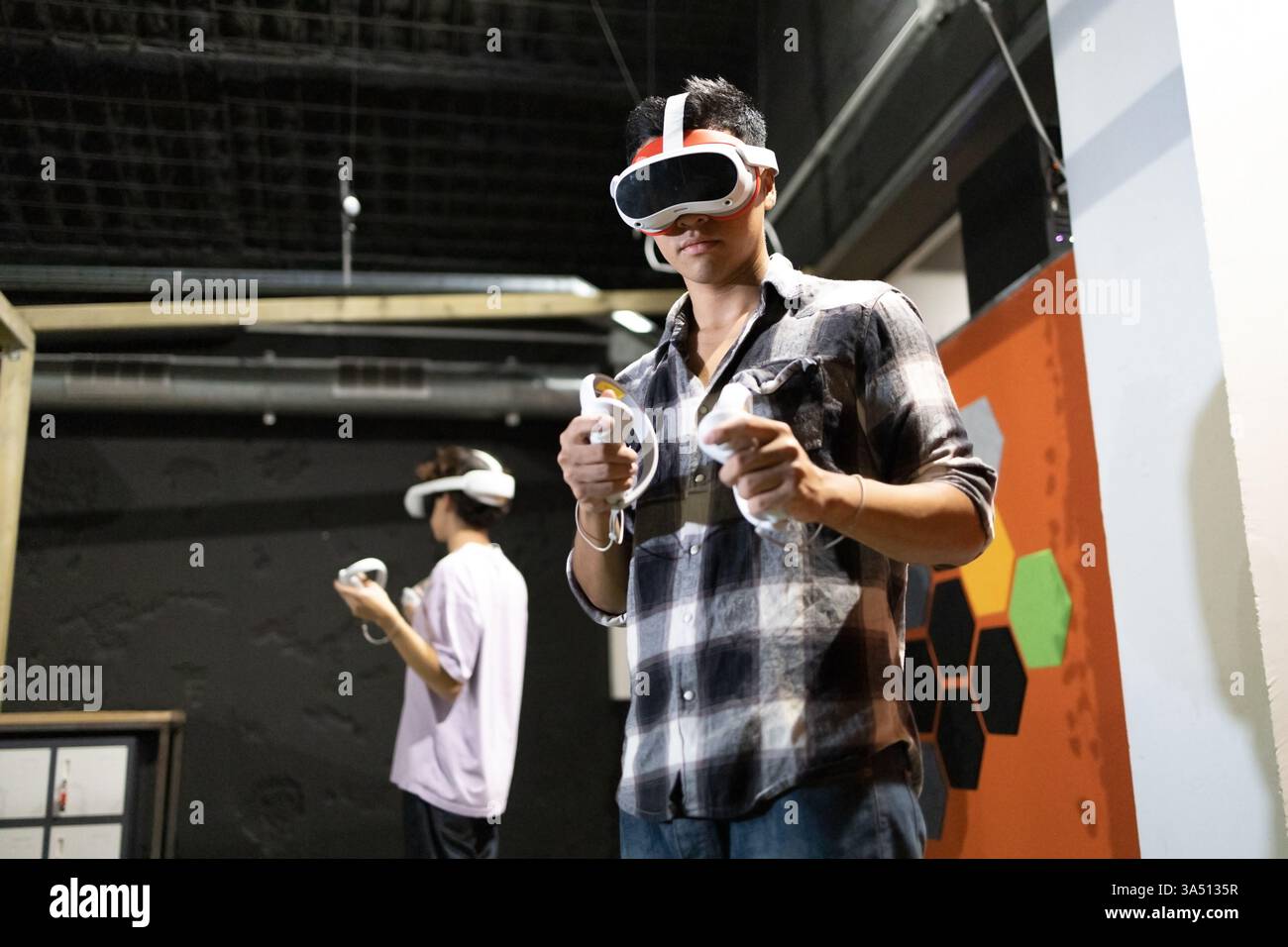 Zwei junge Erwachsene, die sich mit der immersiven virtuellen Realität beschäftigen und VR-Headsets und -Controller in einem Innenbereich tragen. Diese technologieorientierte Szene eignet sich ideal für Spiele, Technologie und digitale Innovationen. Stockfoto