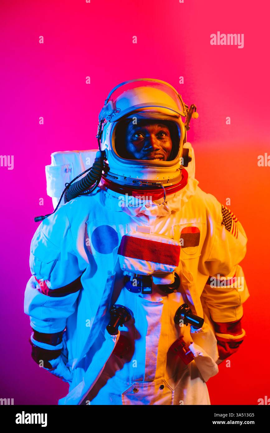 Ein lächelnder Afroamerikaner in einem Weltraumanzug und Helm steht vor einer farbenfrohen Kulisse. Ein fesselndes Porträt, das sich für Themen wie Wissenschaft, Raumfahrt, Bildung oder Technologie eignet. Stockfoto