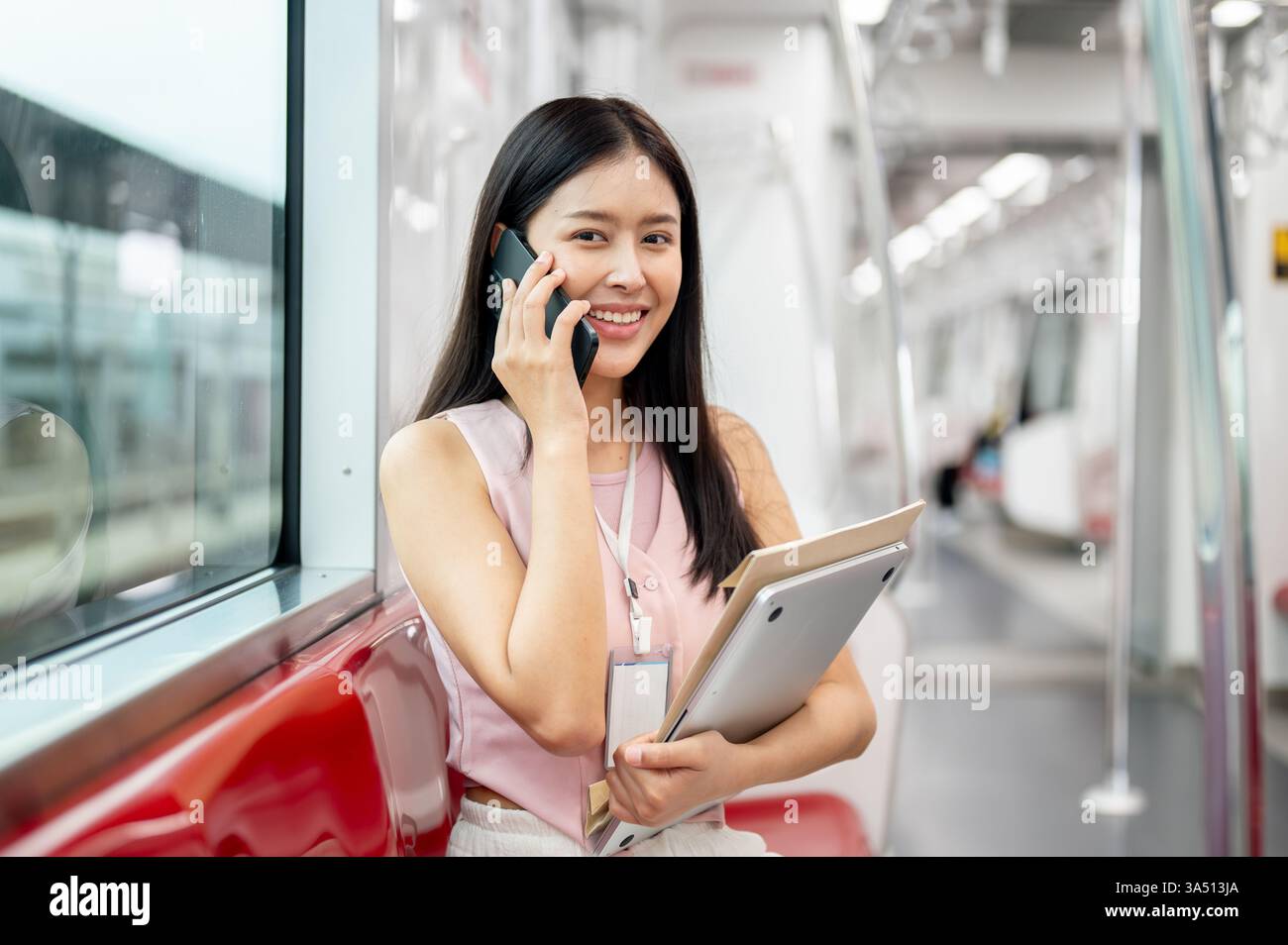 Eine positive asiatische Geschäftsfrau spricht am Telefon, während sie morgens in einem Skytrain pendelt. Die Szene des städtischen Nahverkehrs fängt einen modernen, hoffnungsvollen Start in den Tag ein. Geeignet für Reisen, Pendelfahrten und Konnektivität am Arbeitsplatz. Stockfoto