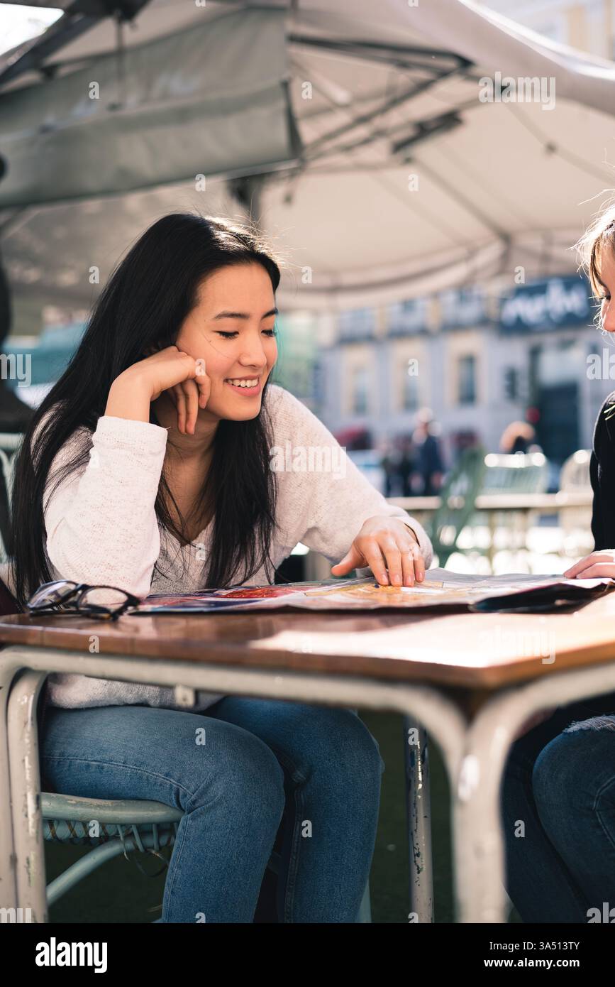 Schöne Gruppe von Freundinnen, die eine Karte auf einer Straße in Madrid studieren, Spanien, sitzen in einem Café. Die Szene fängt Entdeckungen, Freundschaften und urbane Reisen ein. Ideal für Tourismus-, Reise- und Lifestyle-Kampagnen mit multikulturellen Gruppen. Stockfoto