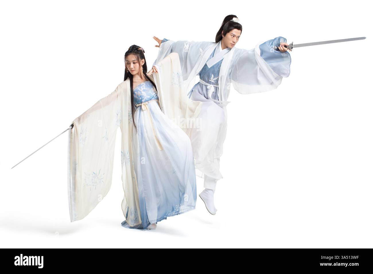 Ein junges chinesisches Paar in traditionellem Hanfu hält Schwerter in einem Atelier vor weißem Hintergrund. Das Bild zeigt die Energie der alten Kostüme und der Kampfkunst, die die traditionelle chinesische Kultur widerspiegelt. Stockfoto