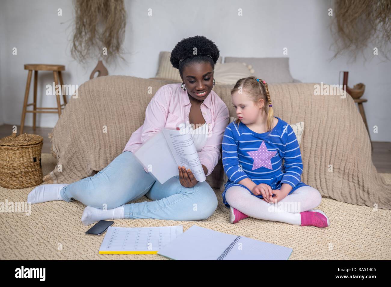 Schwarzes weibliches und weißes Mädchen mit Down-Syndrom, das während des Studiums zu Hause auf dem Boden sitzt Stockfoto