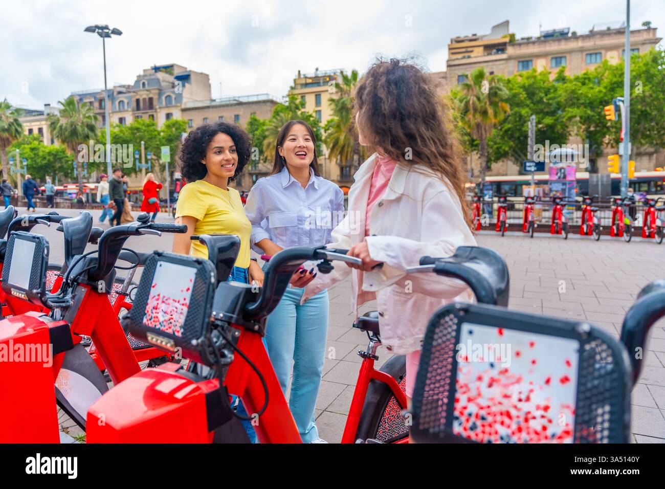 Drei verschiedene Frauen mieten in Barcelona öffentliche Fahrräder, die das Leben in der Stadt und den nachhaltigen Verkehr einfangen. Dieses fröhliche Lifestyle-Image eignet sich für Reisen, Tourismus, städtisches Leben oder umweltfreundliche Mobilitätskampagnen. Ideal für Freundschaft, Kultur und moderne urbane Erlebnisse. Stockfoto