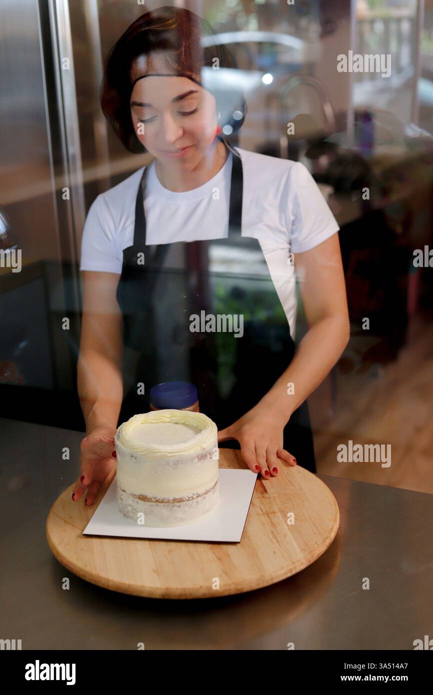 Der konzentrierte Konditor wendet eine Glasur auf einen Kuchen in einer Bäckerei an und präsentiert eine fachkundige Tortendekoration. Perfekt für kulinarische Kunst, Backwaren und Süßwaren. Stockfoto