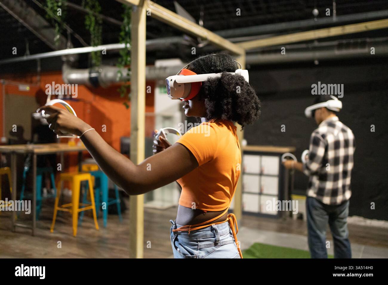 Seitenansicht von zwei jungen multirassischen Freunden, die in Virtual-Reality-Spielen eingetaucht sind, VR-Headsets trugen und Controller in der Hand hielten. In der Technik- und Spieleszene im Innenbereich werden fesselnde Unterhaltung und Social-Media-Spiele beleuchtet. Stockfoto