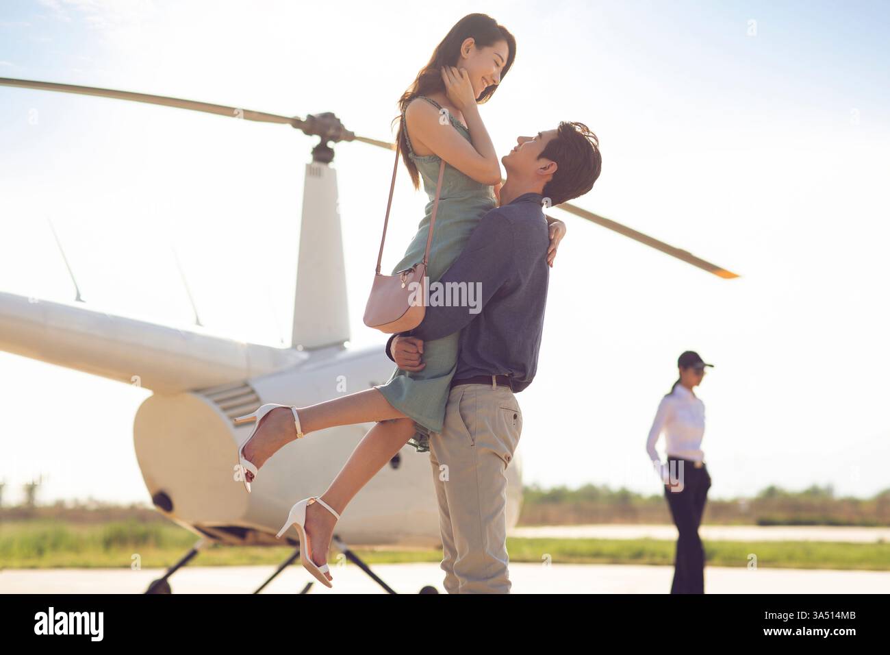 Fröhlicher chinesischer Mann, der seinen Partner bei Sonnenuntergang in der Nähe eines Hubschraubers trägt Stockfoto