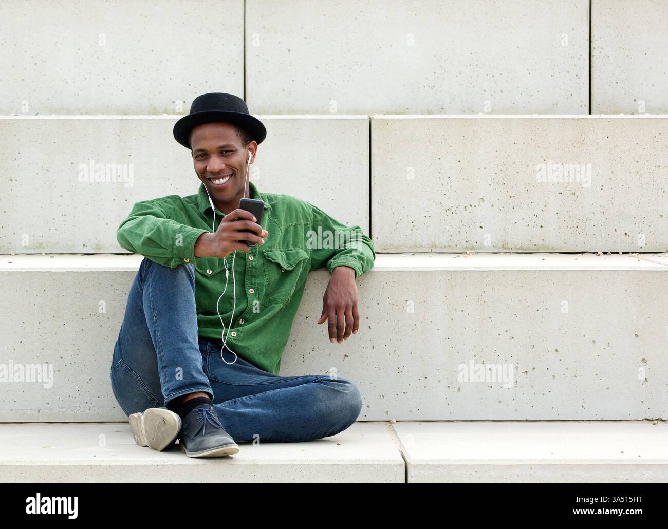 Porträt eines lächelnden Afroamerikaners, der draußen Musik auf seinem Handy genießt. Positives Lifestyle-Image, geeignet für Unterhaltung, Technik und urbane Kampagnen. Ideal für Werbung für mobile Apps und Geräte. Stockfoto