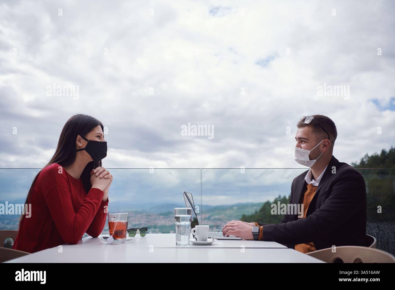 Gruppe von lässig gekleideten Profis im Freien in einem Restaurant, alle tragen Schutzmasken. Sie kooperieren und Brainstorming und veranschaulichen die Teamarbeit in einer modernen Geschäftsszene während der COVID-19-Ära. Stockfoto