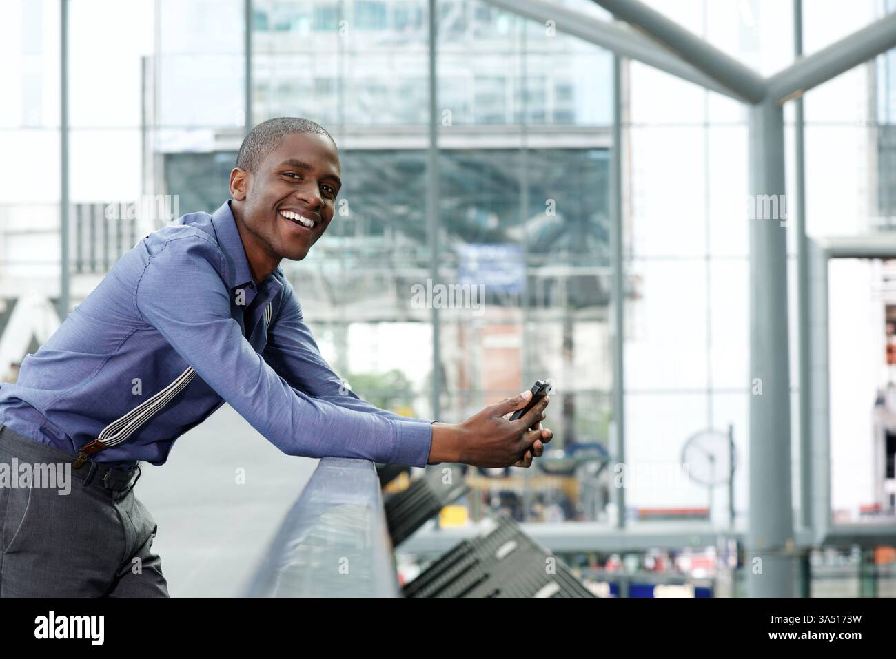 Seitenporträt eines lächelnden schwarzen Geschäftsmannes, der ein Handy hält. Ein selbstbewusster, moderner Profi, ideal für Unternehmenskommunikation, Technologie oder berufsorientierte Inhalte. Dieses Bild vermittelt Zugänglichkeit und Erfolg in einem professionellen Kontext. Stockfoto