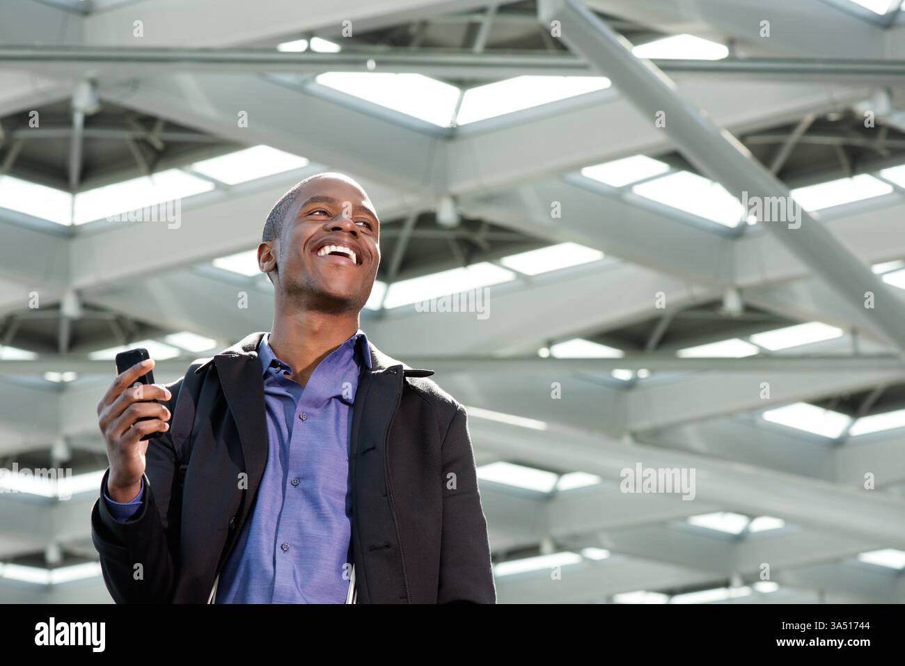 Porträt eines schwarzen Geschäftsmannes, der lacht, während er auf einem Handy spricht. Der ehrliche Moment vermittelt Energie, Zugänglichkeit und professionelles Vertrauen. Perfekt für Unternehmenskommunikation, Visuals für Führungskräfte und Netzwerkthemen. Stockfoto