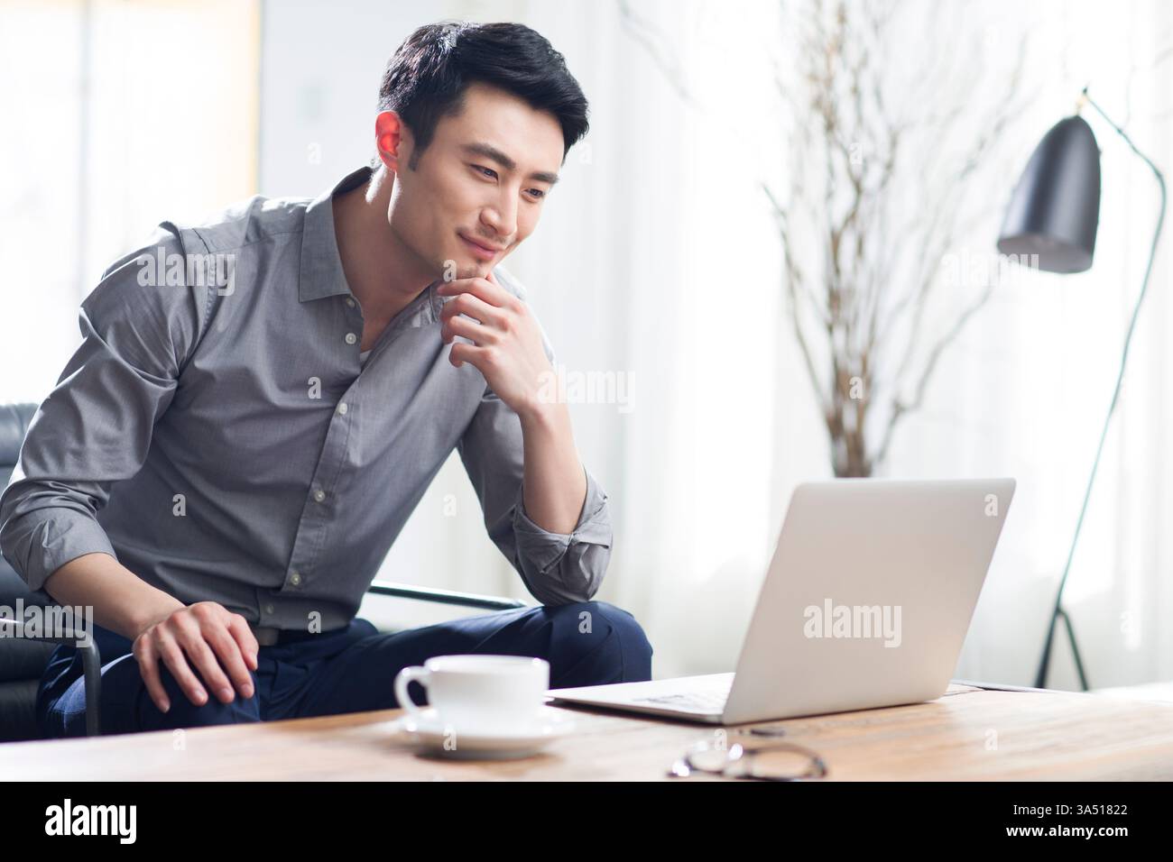 Junger Chinese, der mit Laptop in einem modernen Büro arbeitet. Diese moderne Geschäftsszene legt Wert auf Konzentration, Produktivität und professionellen Stil. Ideal für Unternehmens-, Technologie- und Karrierefunktionen. Stockfoto