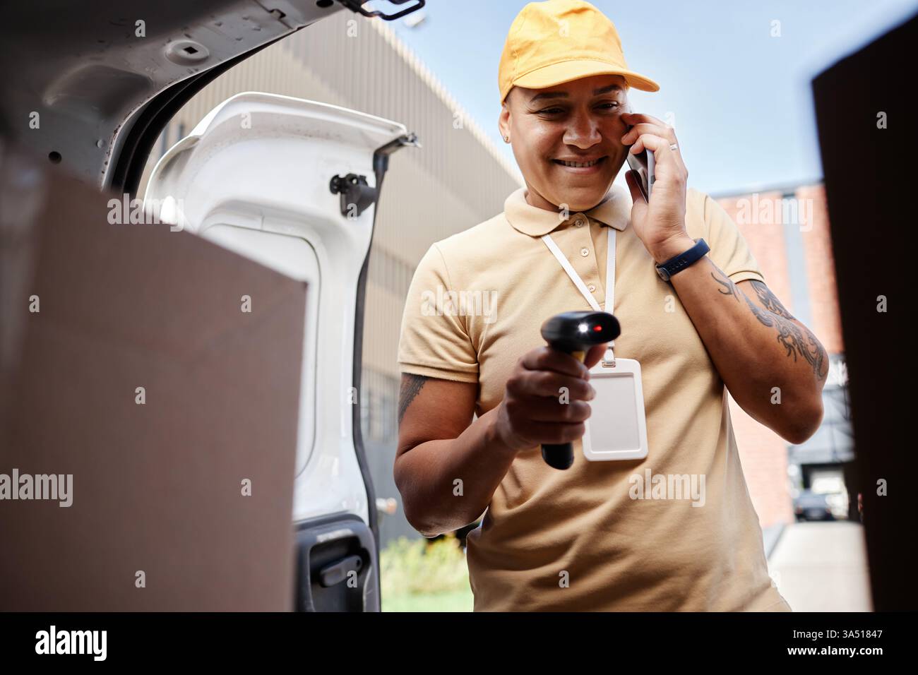 Porträt eines lächelnden Zustellers in einem Lieferwagen, der auf einem Smartphone spricht und Barcodes auf Paketen scannt. In dieser modernen Logistikszene stehen die Rollen E-Commerce, Paketzustellung und Frontline-Service im Vordergrund. Hervorragend geeignet für Geschäftsbereiche, Kurierdienste und technische Außendienste. Stockfoto